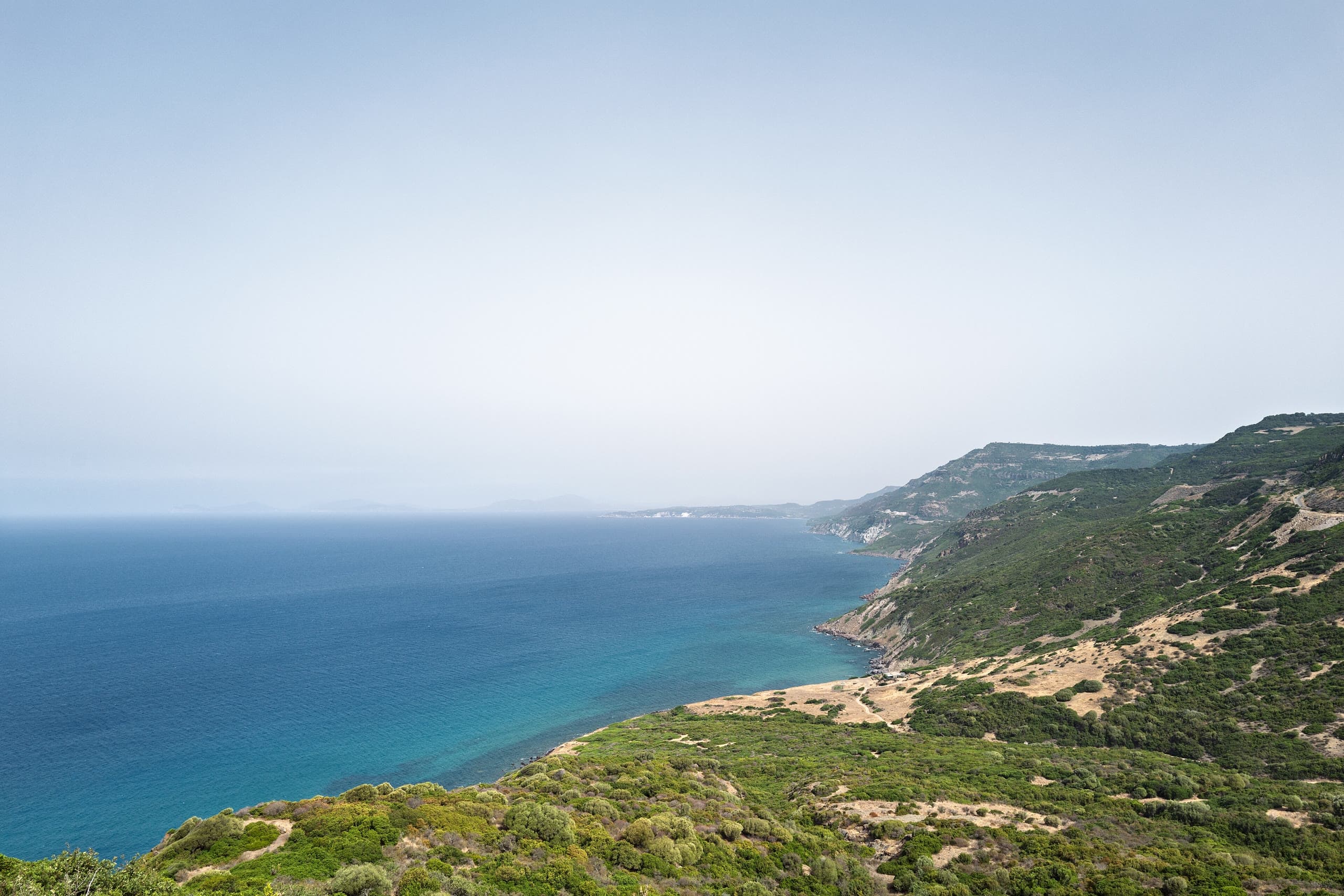 La costa selvaggia tra Alghero e Bosa: acqua turchese sotto promontori verdi e la strada tagliata nella roccia