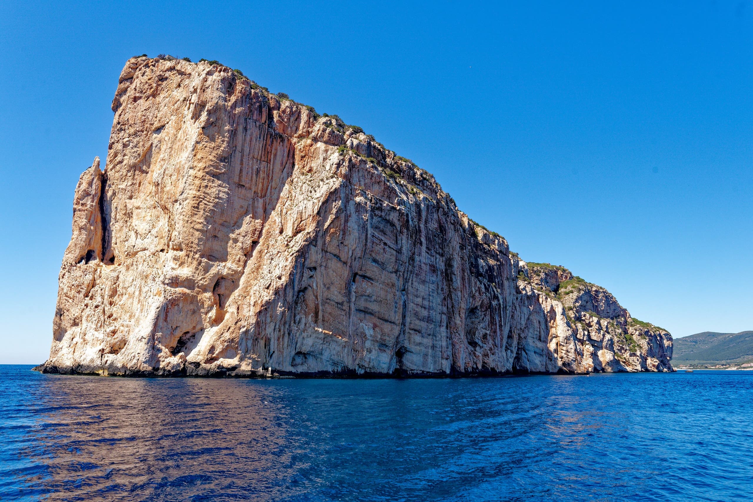 The limestone cliff of Capo Caccia rising straight out of deep blue water, photographed from a boat offshore.