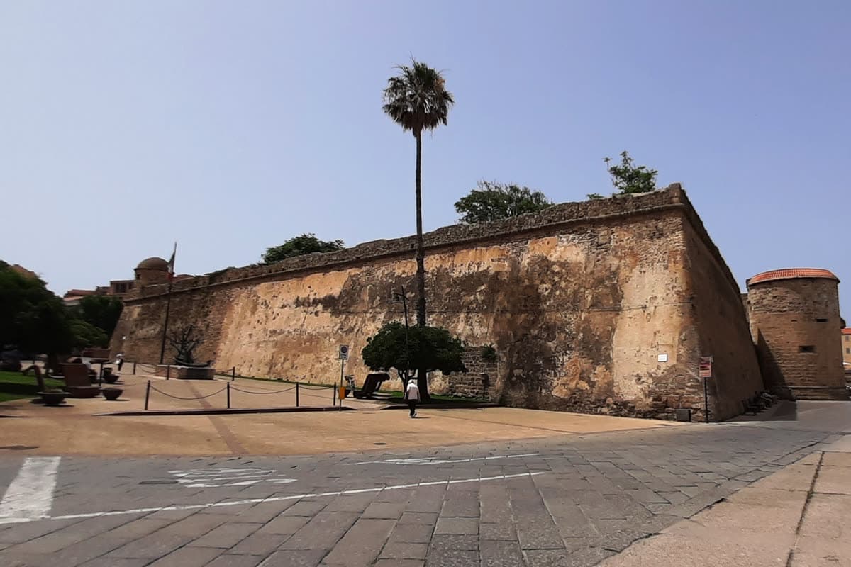 The low stone wall of the Maddalena bastion in Alghero with a palm tree above it