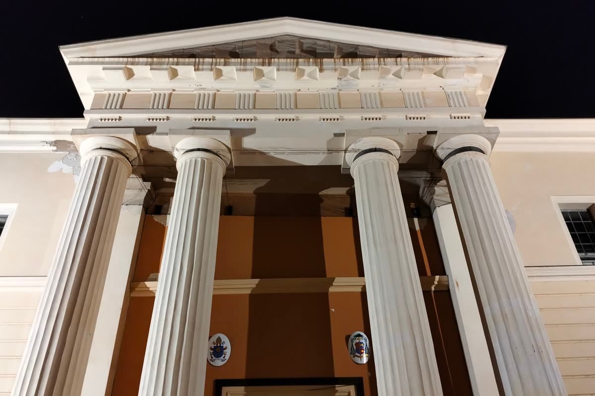 The neoclassical portico of Alghero cathedral at night, seen from below between fluted Doric columns