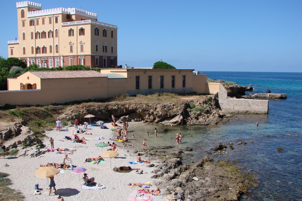 Villa Las Tronas on its headland above the sea near Alghero, with a small beach and bathers below