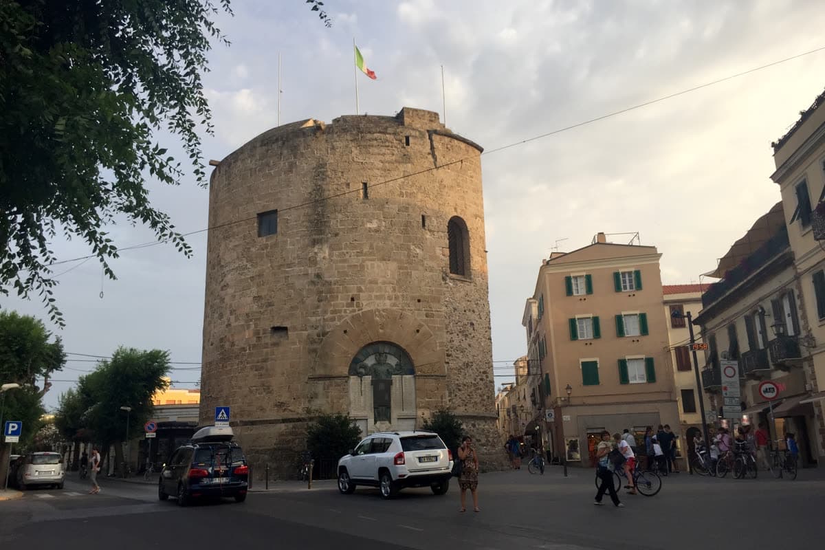 The round stone tower of Porta a Terra in Alghero, standing free between the modern buildings of the square