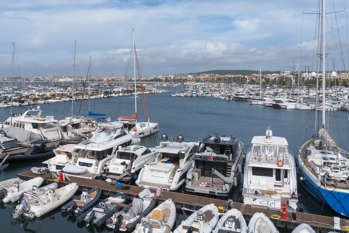 Yachts and fishing boats moored in the harbour of Alghero under a bright sky