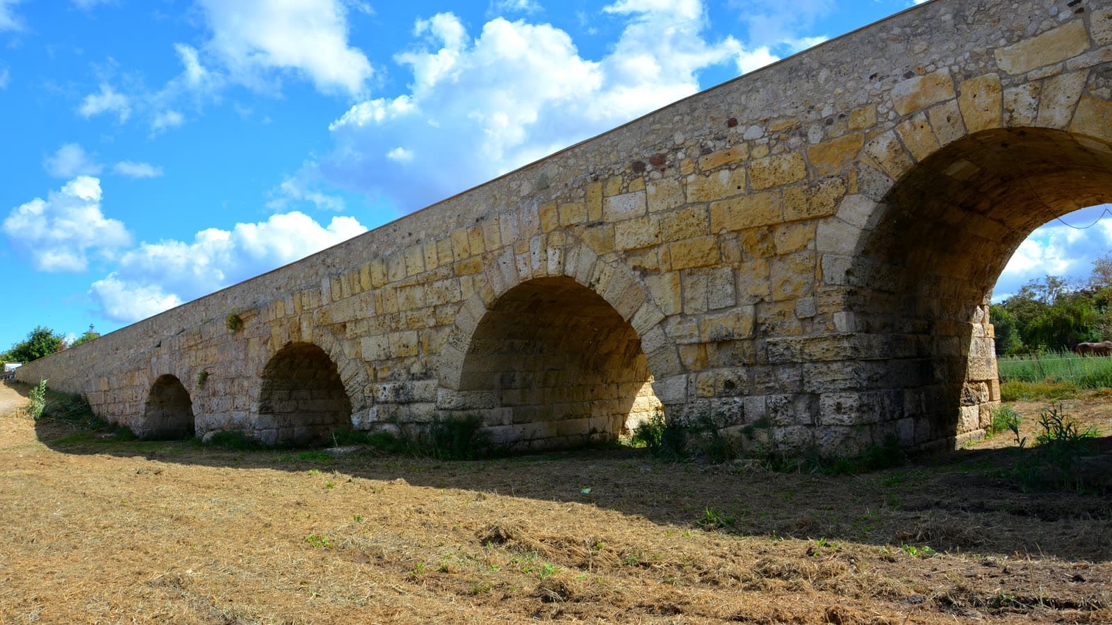 Il ponte romano di Porto Torres, sette arcate in pietra sopra il terreno asciutto sotto un cielo azzurro