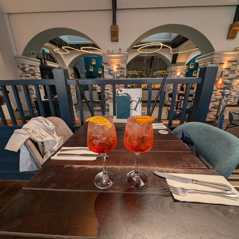 Two Aperol spritzes on a laid table in a dining room