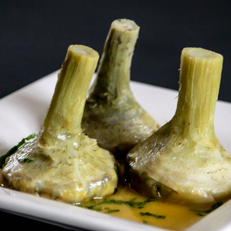 Artichokes braised whole, stems upward, on a white plate