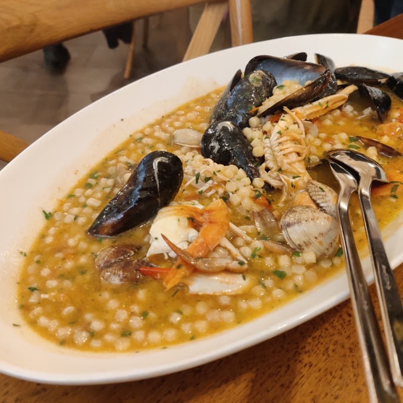 A plate of fregola with mussels, prawns and squid in a shallow broth, photographed in Alghero