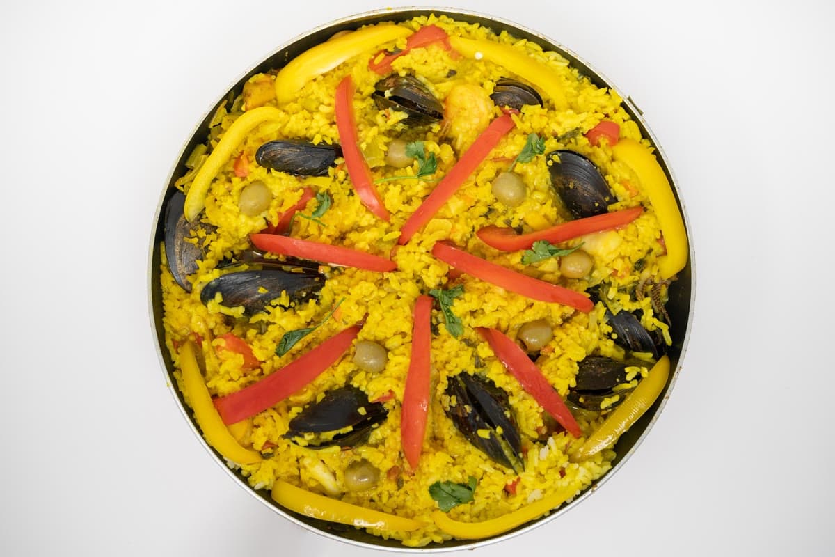 A seafood paella seen from above: saffron rice with prawns, mussels and strips of red pepper