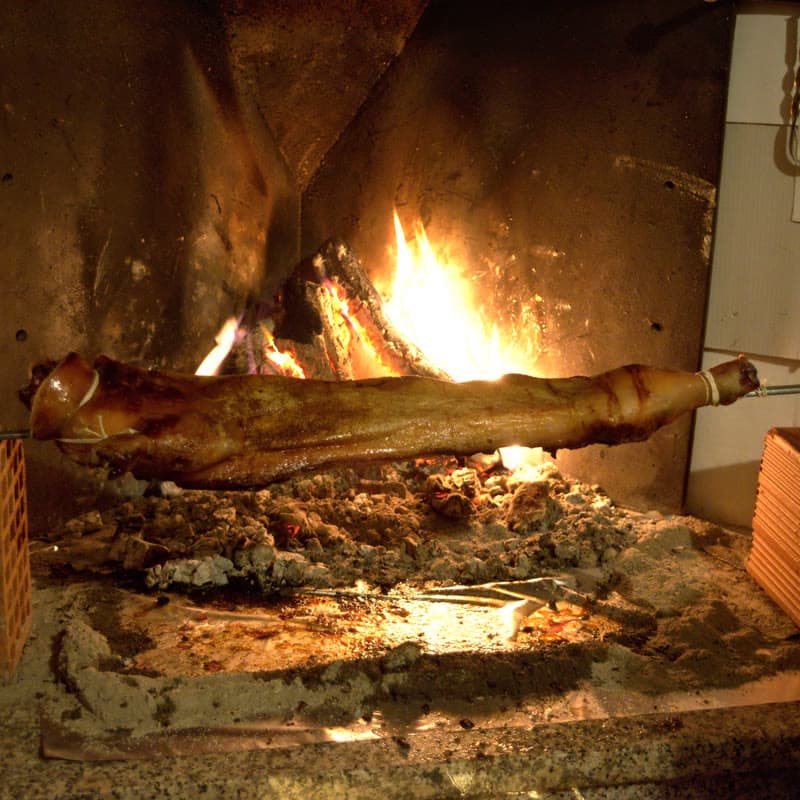 A suckling pig on a spit turning in front of an open wood fire