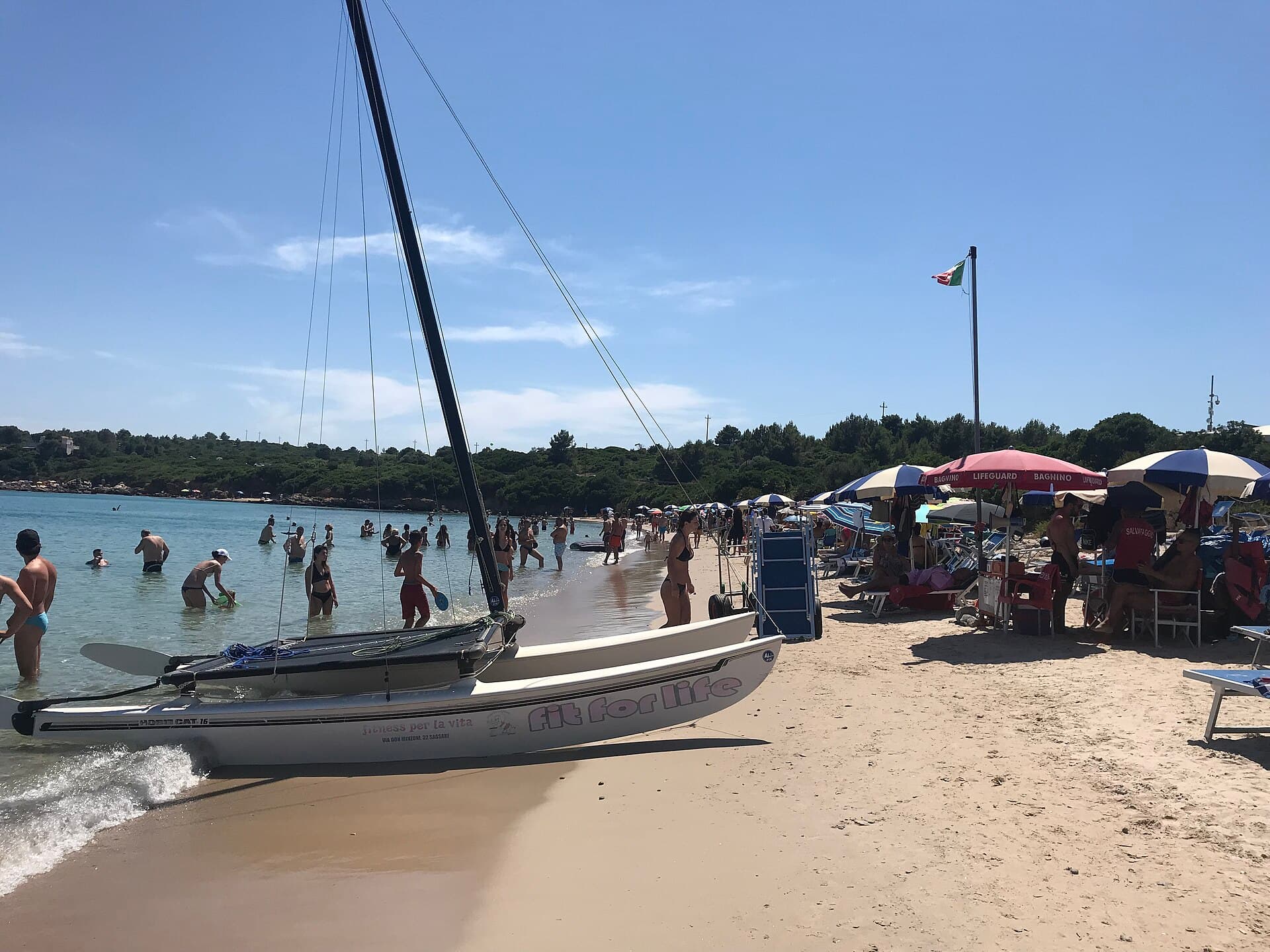 Sunny turquoise cove at Lazzaretto beach with a small catamaran on the sand