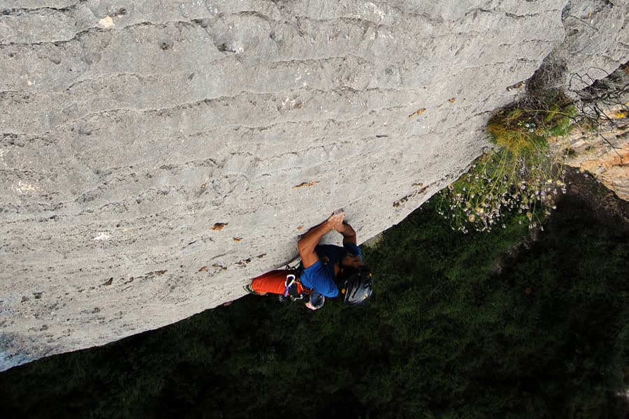 A climber on a smooth overhanging limestone wall, seen from above.