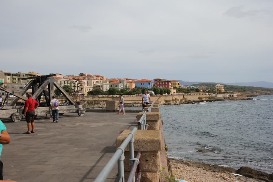 People walking along the seafront promenade in Alghero, with the old town behind.