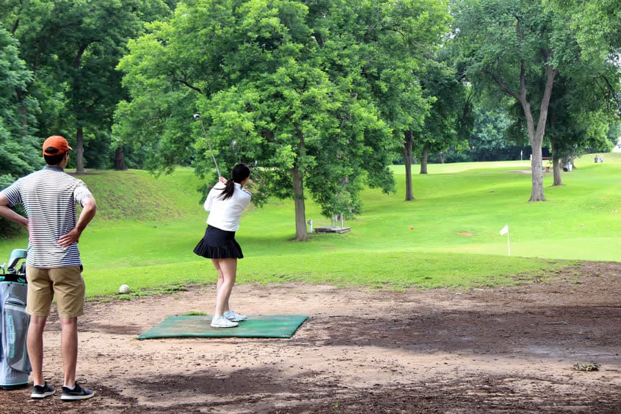 Players on the tee of a short pitch and putt course among trees.