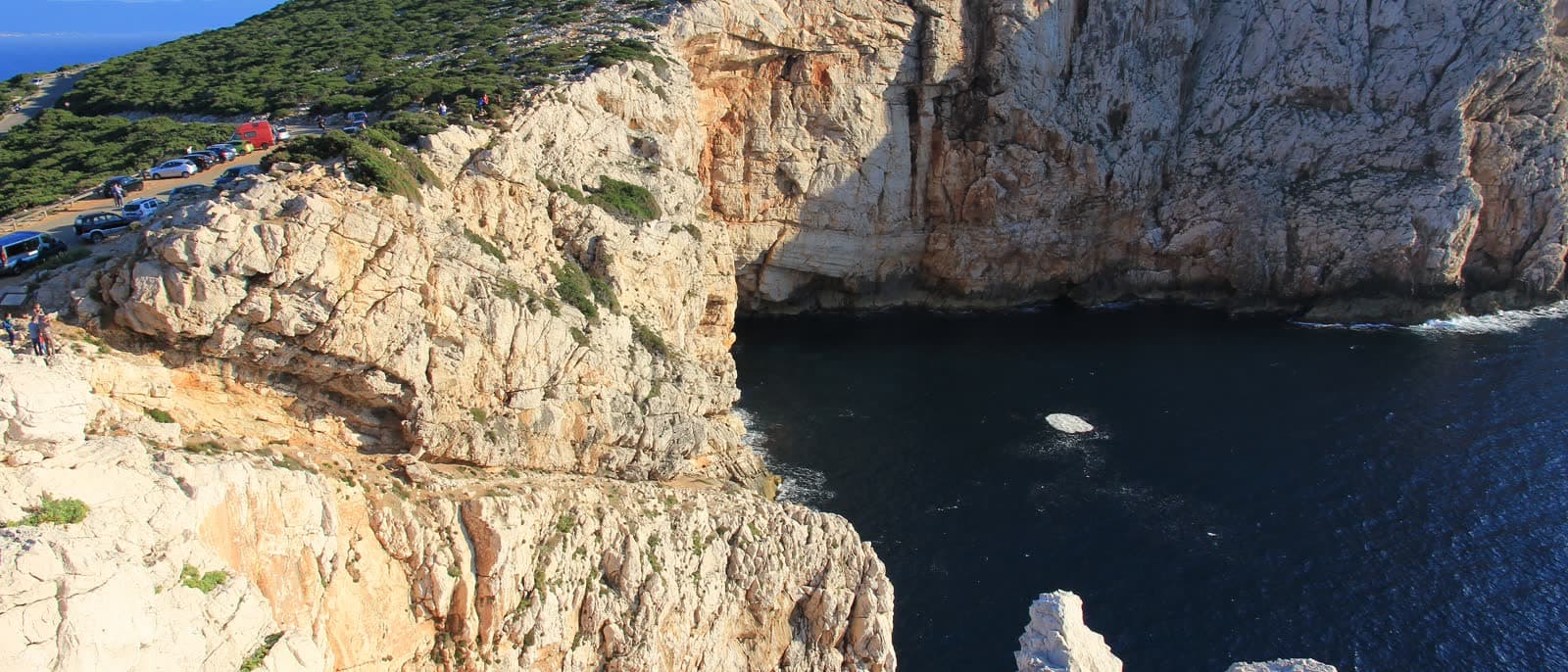 The limestone walls of Capo Caccia seen from above, with a cove at their foot.