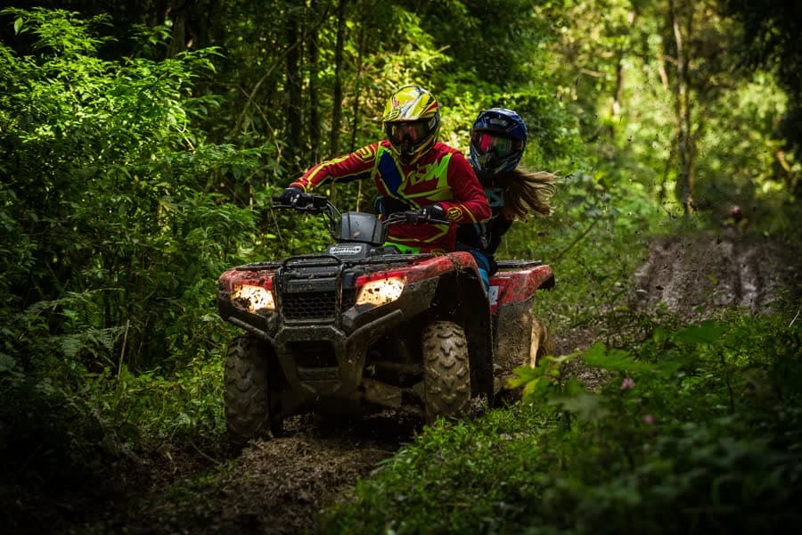Two people in helmets riding a quad along a forest track.