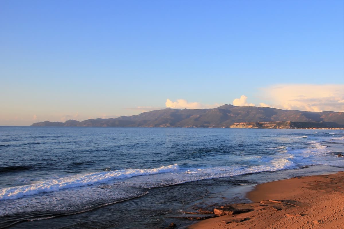 Capo Marrargiu at dusk: a dark headland above a pale sea on the wild coast south of Alghero.
