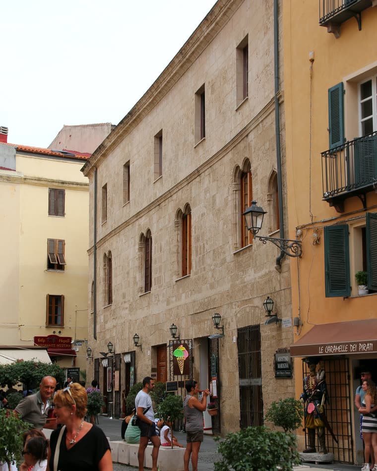 Die Steinfassade des Palazzo d'Albis an der Piazza Civica in Alghero mit katalanisch-gotischen Doppelfenstern über den Geschäften des Platzes