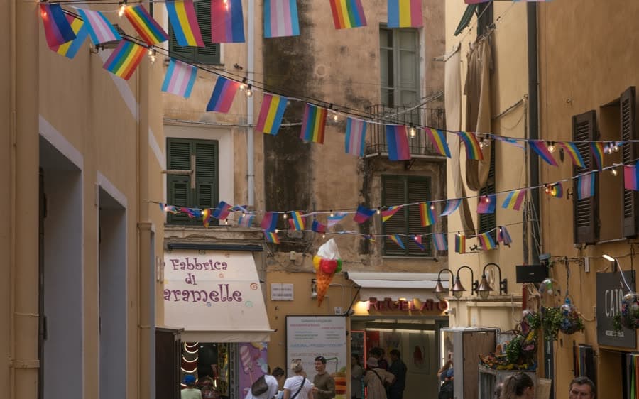 Eine enge Gasse der Altstadt von Alghero mit hohen Steinhäusern und Wimpeln