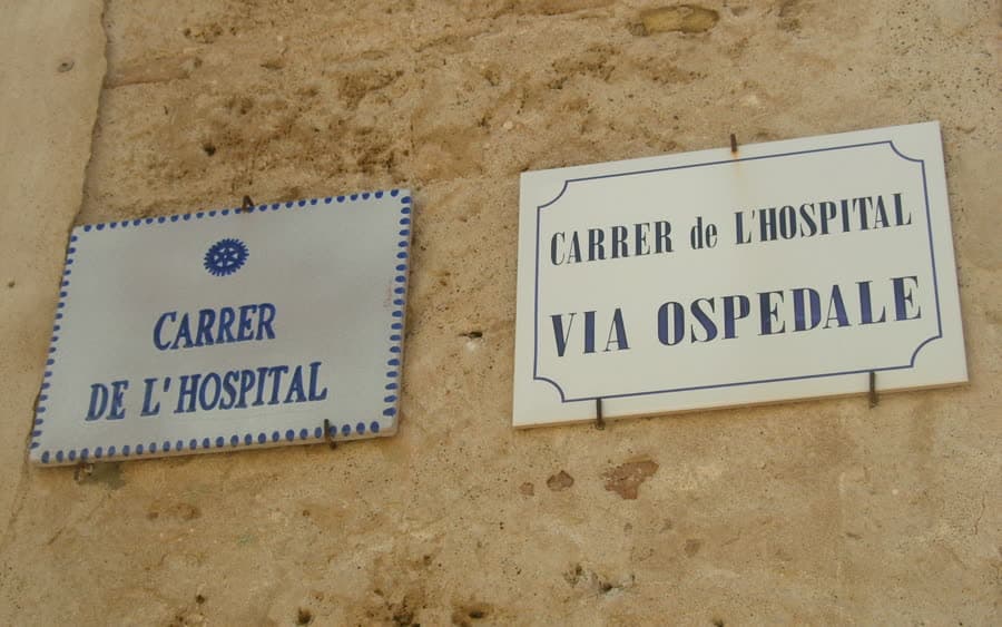 Zwei Straßenschilder an einer Ecke in Alghero, eines auf Italienisch, eines auf Katalanisch