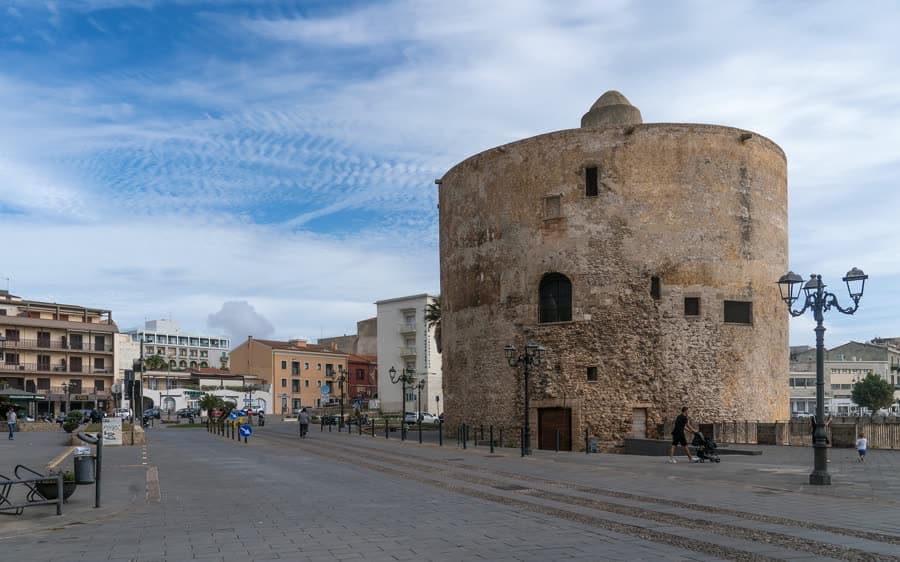 Der runde Steinturm Torre di Sulis an der Uferpromenade von Alghero unter blauem Himmel
