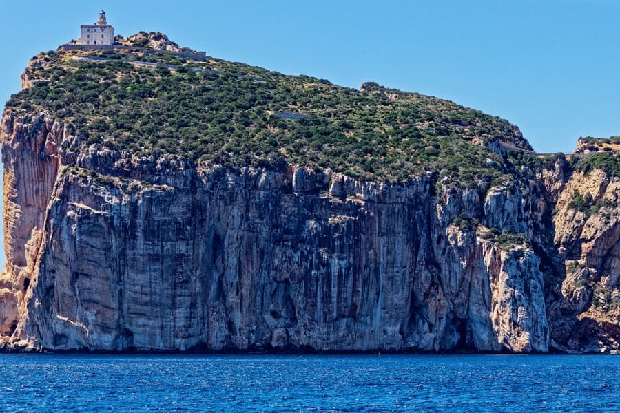 The headland of Capo Caccia rising from deep blue sea, the lighthouse on top.