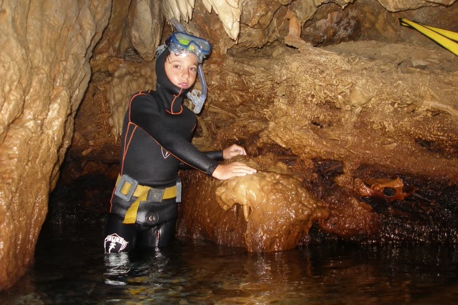 A diver in a wetsuit beside fossil deer bones in an underwater cave at Punta Giglio.