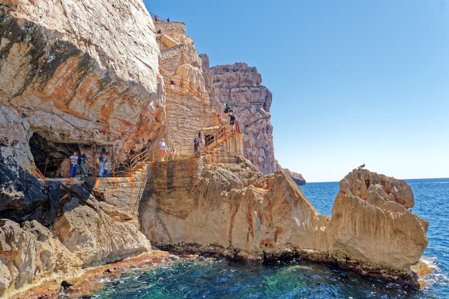 The cliff at Capo Caccia seen from the water, the Escala del Cabirol staircase cut into the rock above the cave mouth.