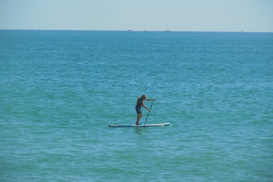 A person standing on a paddleboard on flat open water.