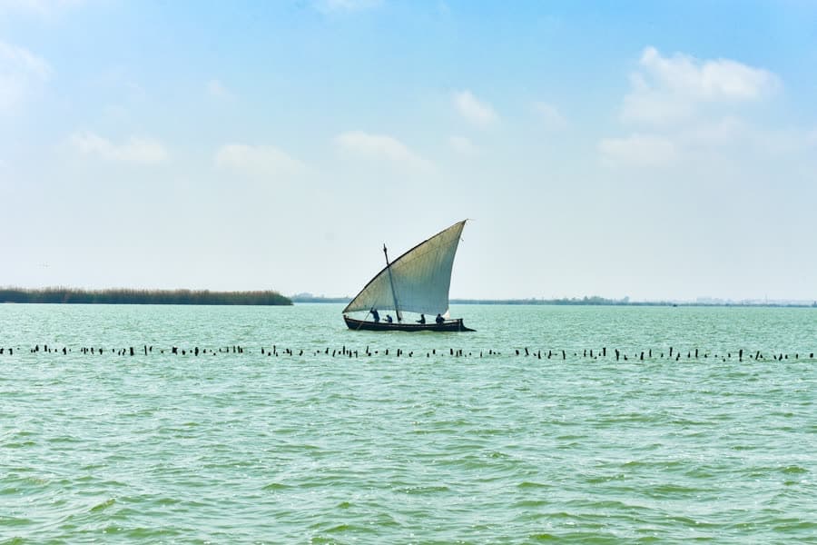 A boat under a single triangular lateen sail on a shallow lagoon.