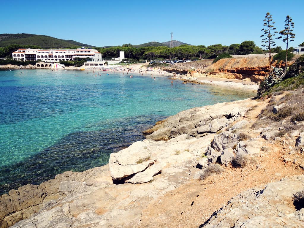 Agua turquesa en la cala resguardada de Punta Negra cerca de Fertilia, con losas de caliza y bañistas junto a la arena